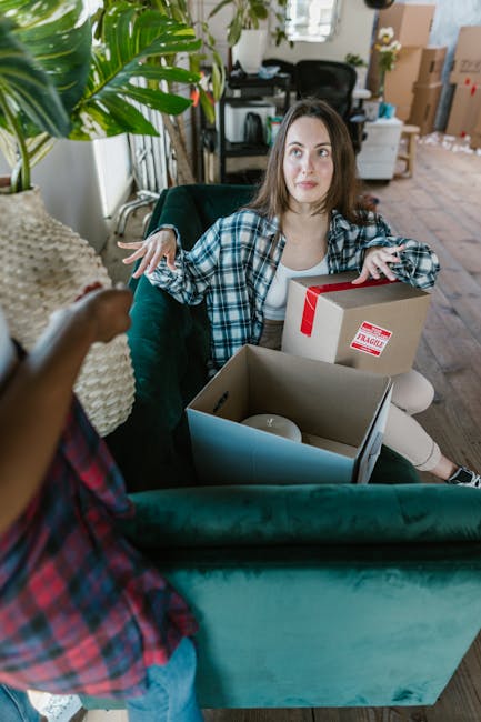 The image displays a close-up view of the inside of a household moving process, with several cardboard boxes and packing materials visible. A partially visible open cardboard box is positioned on a fl