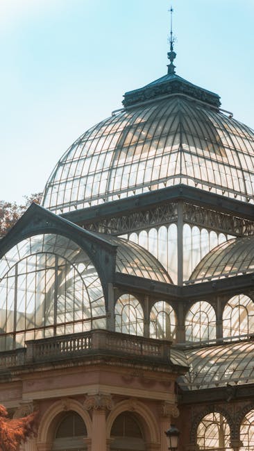 A scenic view of Crystal Palace Park featuring a large pond in the foreground with surrounding greenery including bushes and trees on both sides. In the background, the iconic glass and steel Crystal Palace building is visible, characterized by its domed roof and classical architectural features, situated behind the pond. A central fountain sprays water upward from the pond's surface, and a group of people can be seen near the building’s entrance. The sky above is partly cloudy with patches of blue, and the environment appears calm and well-maintained, suitable for leisurely activities. This image captures the tranquil setting ideal for house removals or relocation services near Crystal Palace, emphasizing the natural surroundings and architectural landmarks relevant to local moves facilitated by [COMPANY_NAME].